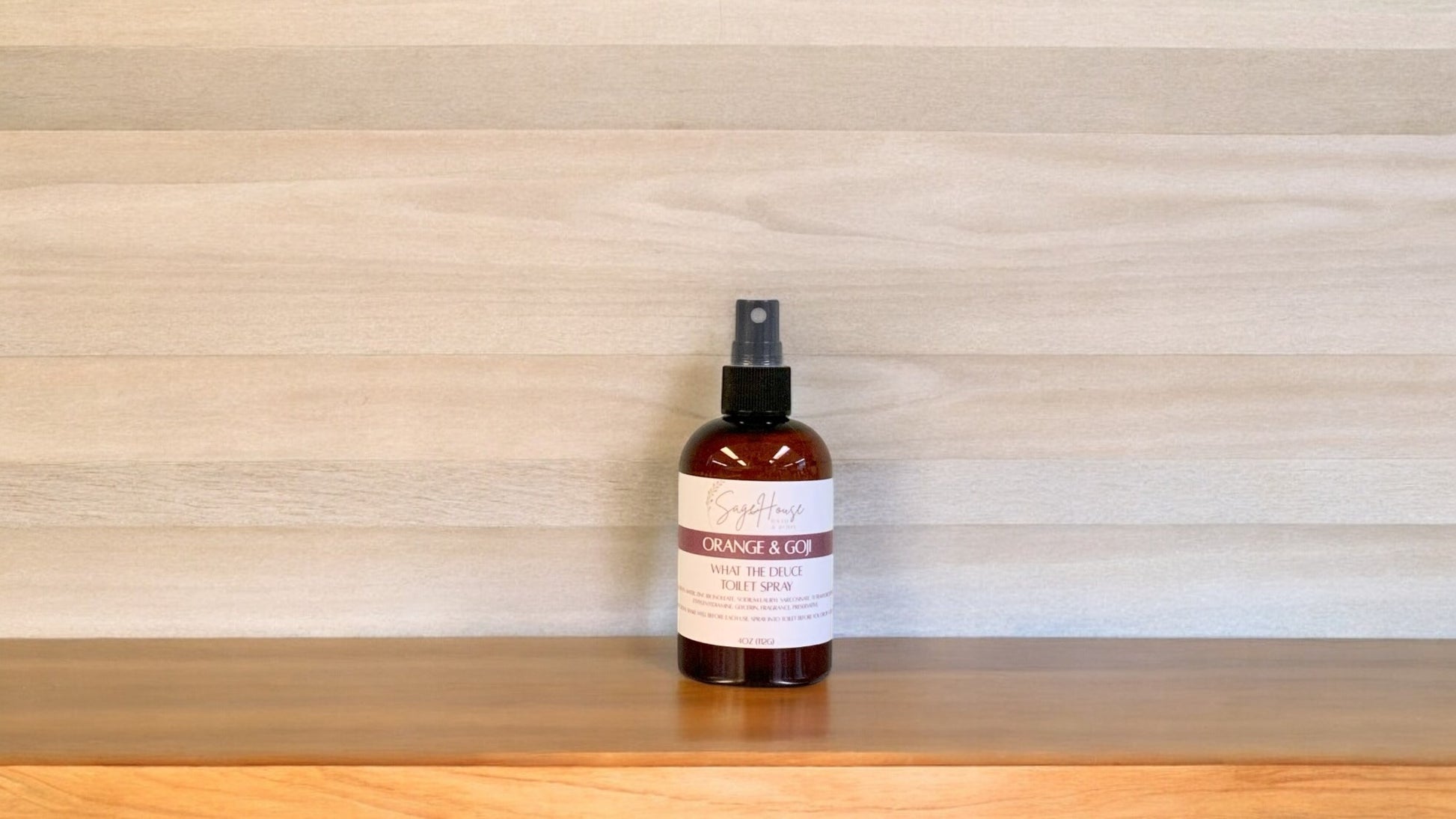 Amber colored spritz bottle with orange and goji label, on wood surface