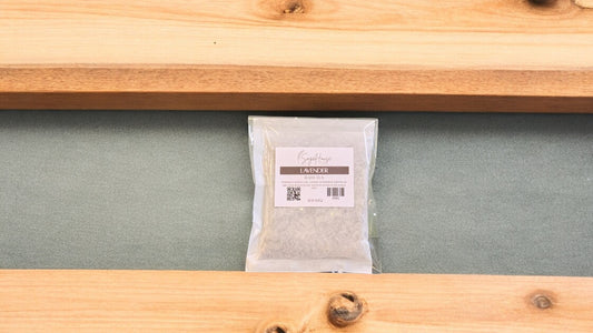 A large bath tea bag inside of a package. Sitting on a wood surface against a sage green background
