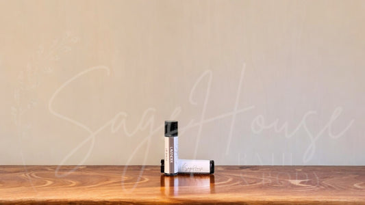A tube of lavender lip balm placed upright with a tube lying behind it, on a wooden surface.