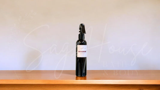 Black spray bottle with a label, on a wooden surface against a white textured wall.
