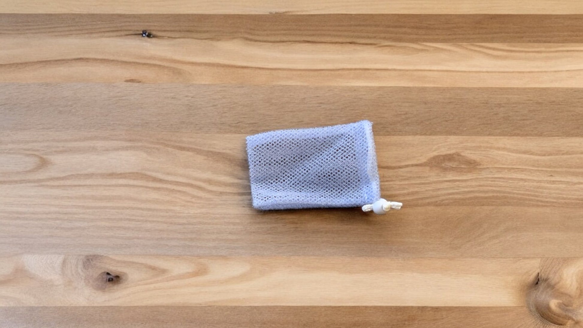 A Soap Scrub Pouch in lavender, placed on a wooden surface.