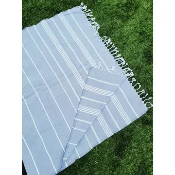 Light Blue Turkish cotton towel, folded onto itself, on grass, on a white background.