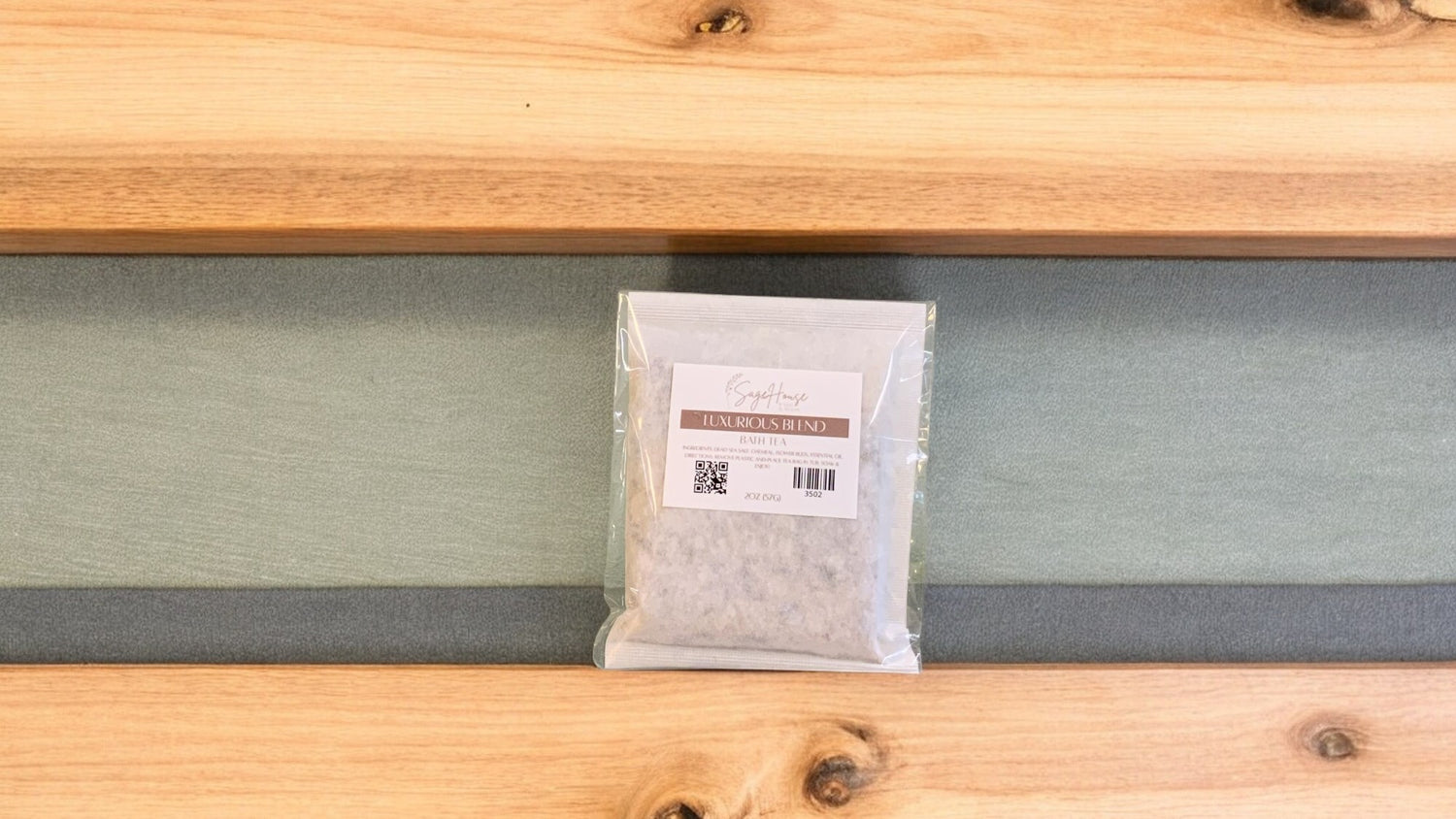 A large bath tea bag inside of a package. Sitting on a wood surface against a sage green background