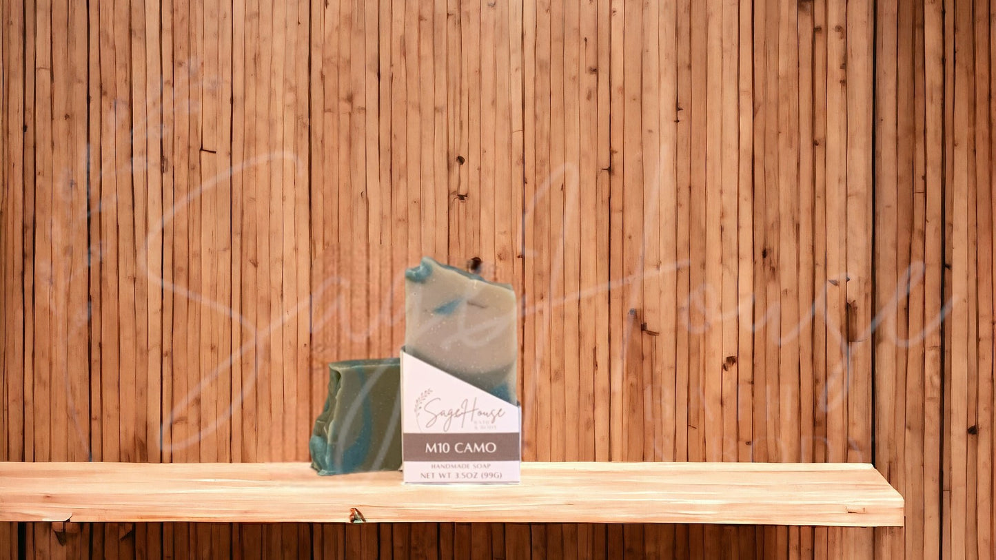 A tan colored bar of soap with dark brown and dark green accents with a white label. on a wood surface.