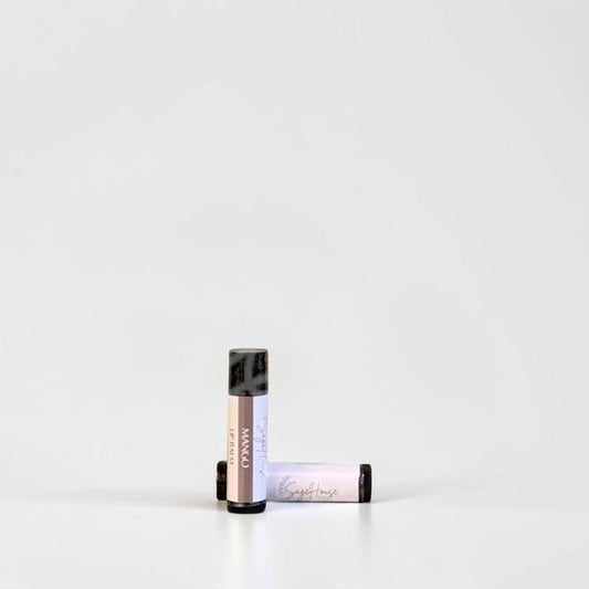 Two slim cylindrical lip balm tubes, one standing upright and one lying horizontally, positioned near the center of a clean white studio background.