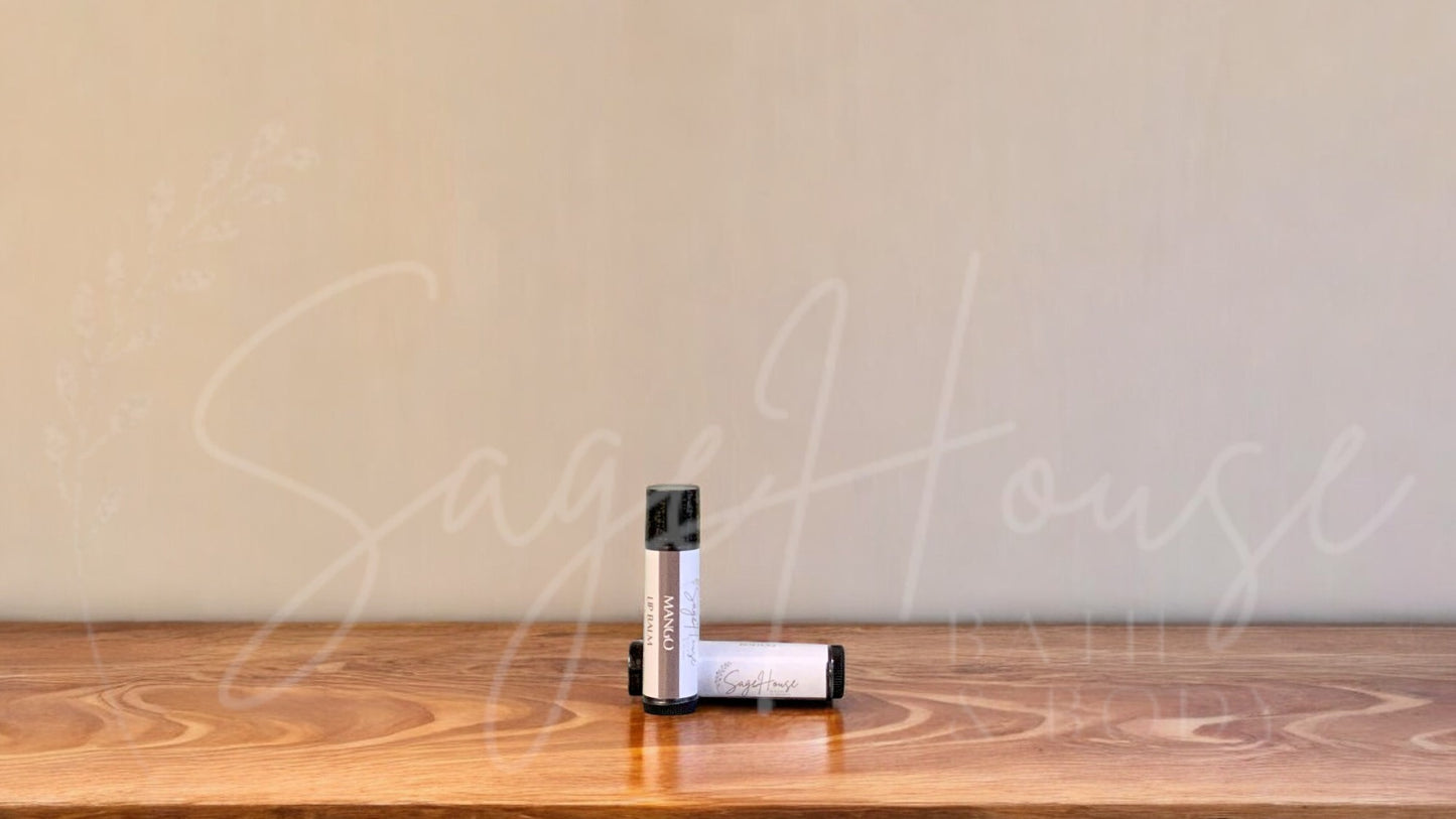 A tube of mango lip balm placed upright with a tube lying behind it, on a wooden surface.