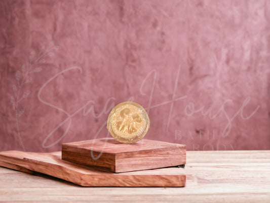 A tan colored bar of oatmeal milk and honey loofah soap resting on a wooden soap dish, with a pink background.