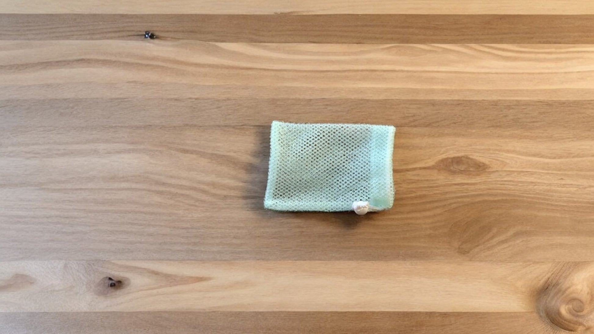 A Soap Scrub Pouches in ocean blue placed on a wooden surface.