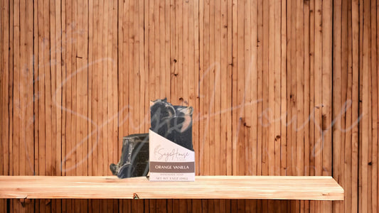 A black colored bar of soap with orange accents with a white label. on a wood surface.