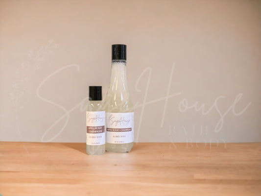A bottle of Sage House bubble bath, labeled 'apple honey champagne'. Placed on a wooden surface.