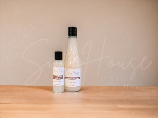 A bottle of Sage House bubble bath, labeled 'black raspberry vanilla'. Placed on a wooden surface.