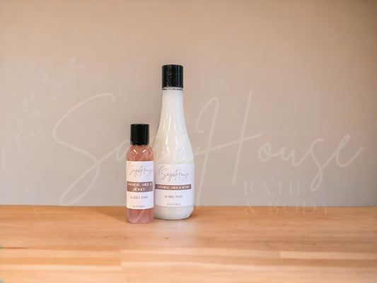 A bottle of Sage House bubble bath, labeled 'oatmeal milk and honey'. Placed on a wooden surface.