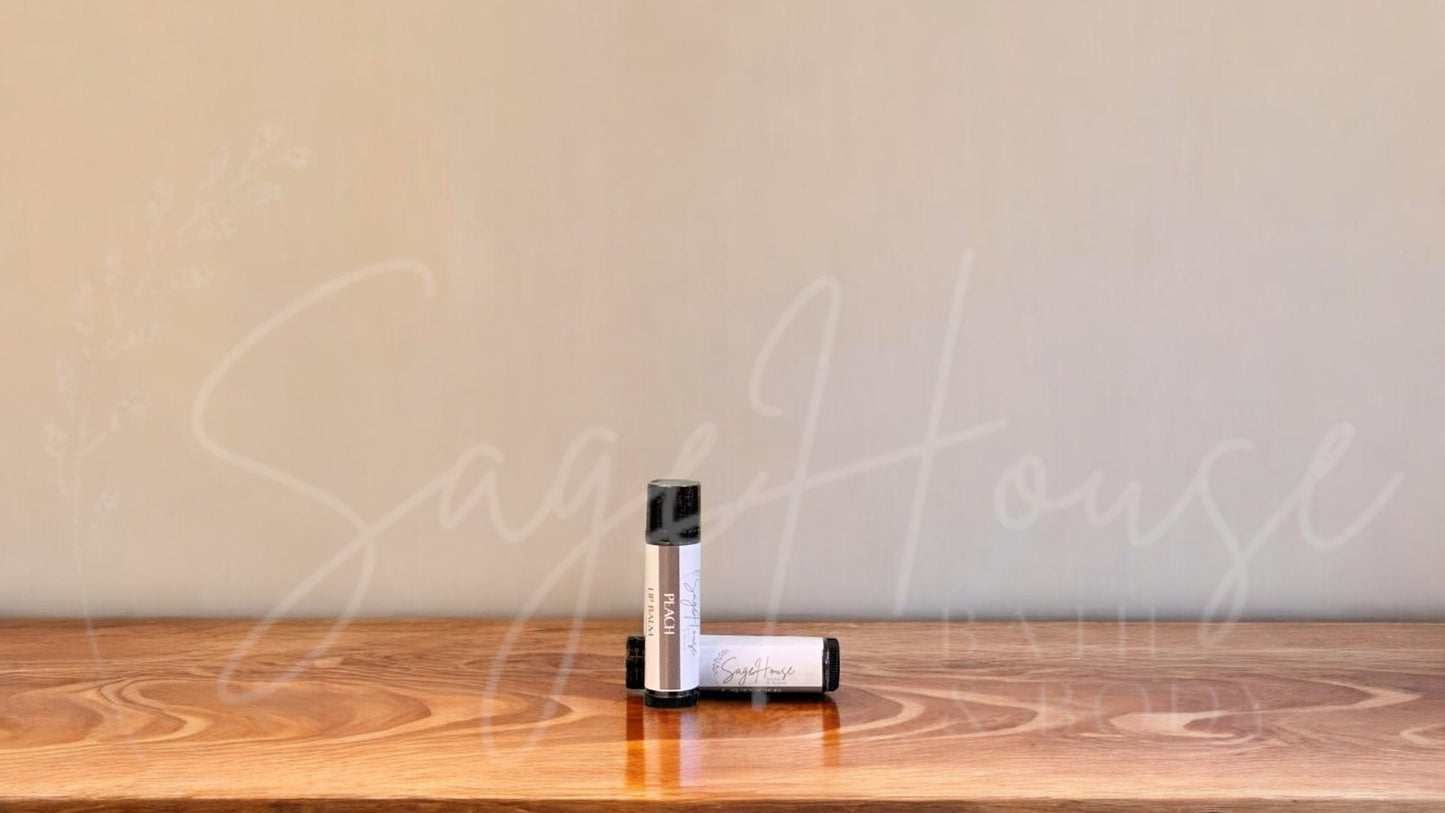 A tube of peach lip balm placed upright with a tube lying behind it, on a wooden surface.