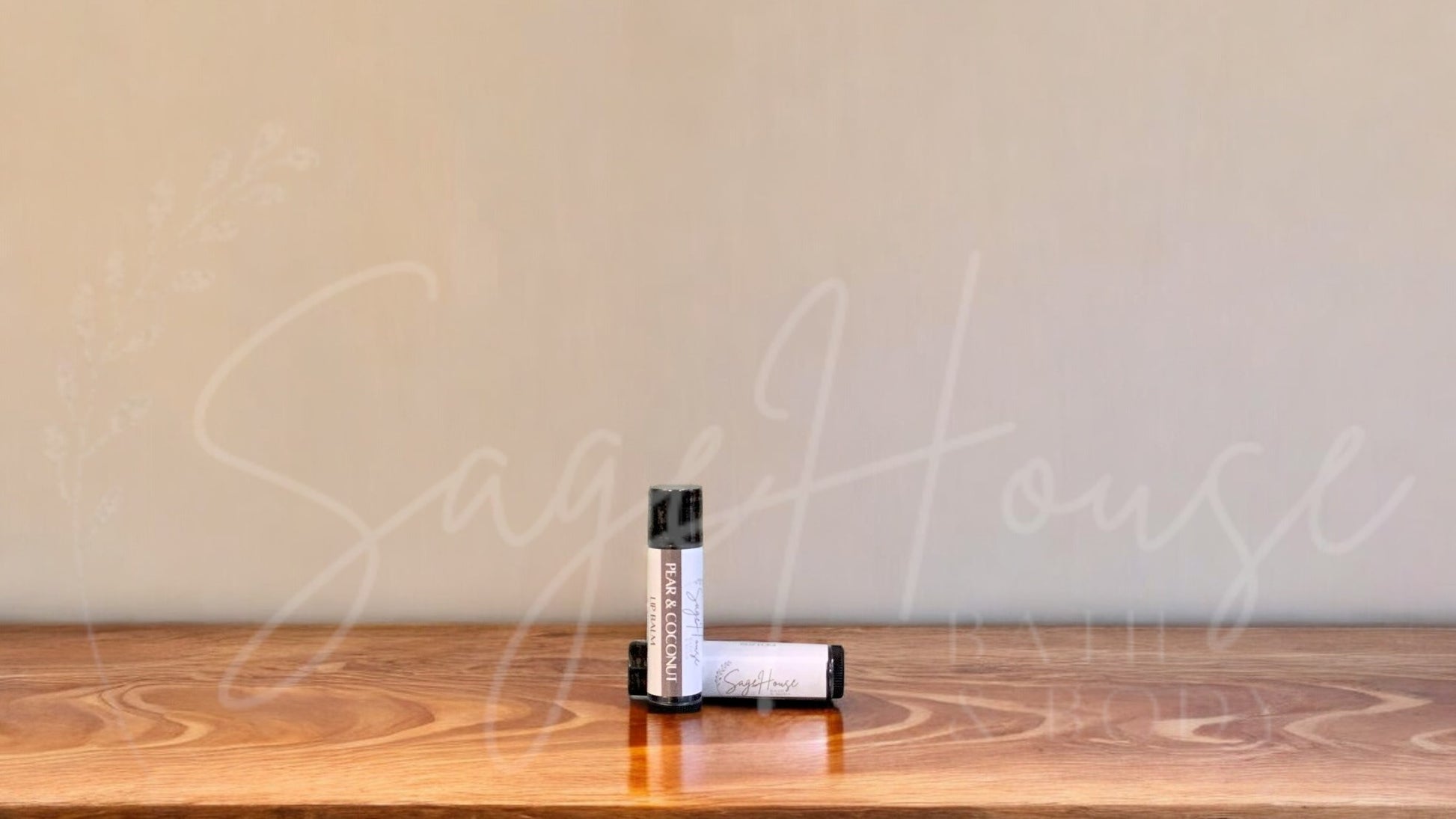 A tube of pear and coconut lip balm placed upright with a tube lying behind it, on a wooden surface.