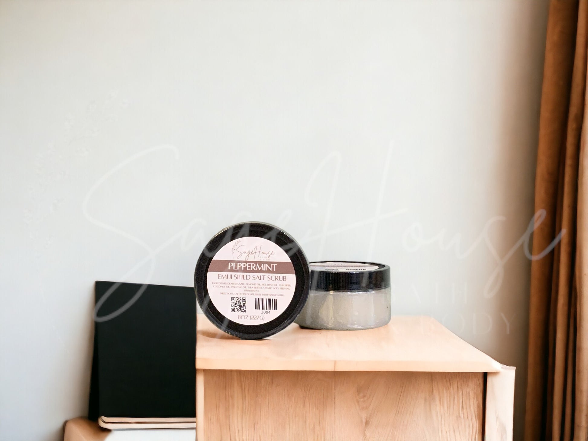 Two jars of scrub, one standing next to the other, sitting on a wooden surface with a white background