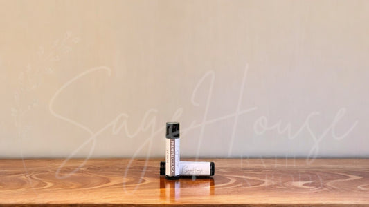 A tube of pineapple colada lip balm placed upright with a tube lying behind it, on a wooden surface.