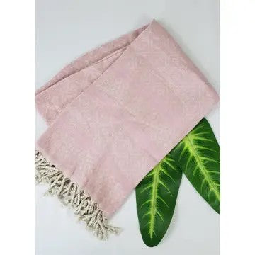 Pink Turkish cotton towel with diamond pattern, folded onto itself, with 2 leaves underneath, on a white background.