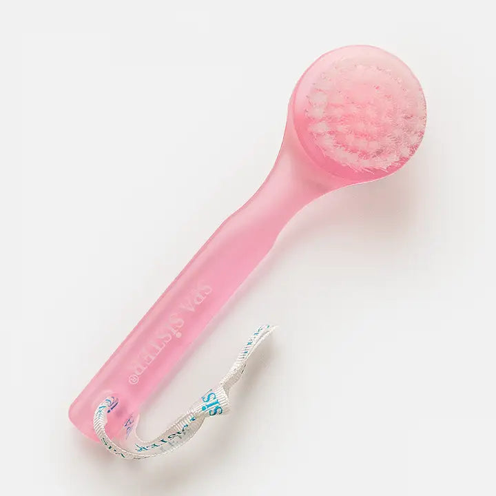 A pink facial cleansing brush with string. On white background