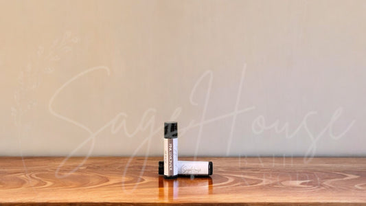 A tube of pink lemonade lip balm placed upright with a tube lying behind it, on a wooden surface.