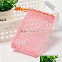 A Soap Scrub Pouch in pink, placed on a white surface. A basket and plant in the background.