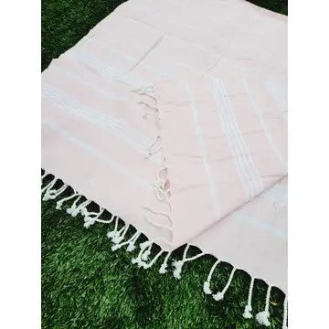Pink Turkish cotton towel, folded onto itself, on grass, on a white background.
