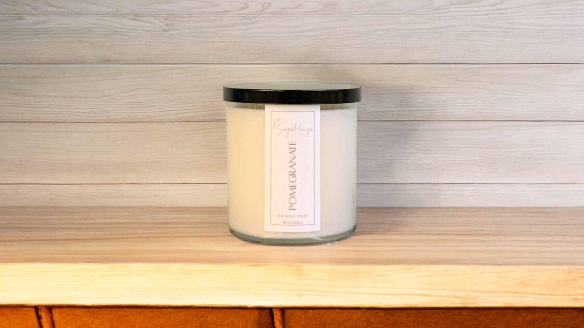 A white soy wax candle in a clear container, placed on a wooden surface, with a label on the front.