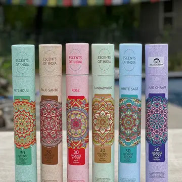 A collection of incense sticks in various colors, each labeled with different scents such as 'Patchouli', 'Rose', 'Sandalwood', "Nagchampa" and 'White Sage'. The incense sticks are displayed in a patterned tray, with a pool and trees in the background.