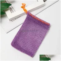 A Soap Scrub Pouch in purple, placed on a white surface. A basket and plant in the background.