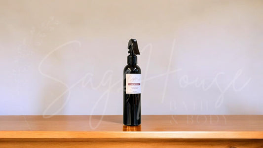 Black spray bottle with a label, on a wooden surface against a white textured wall.