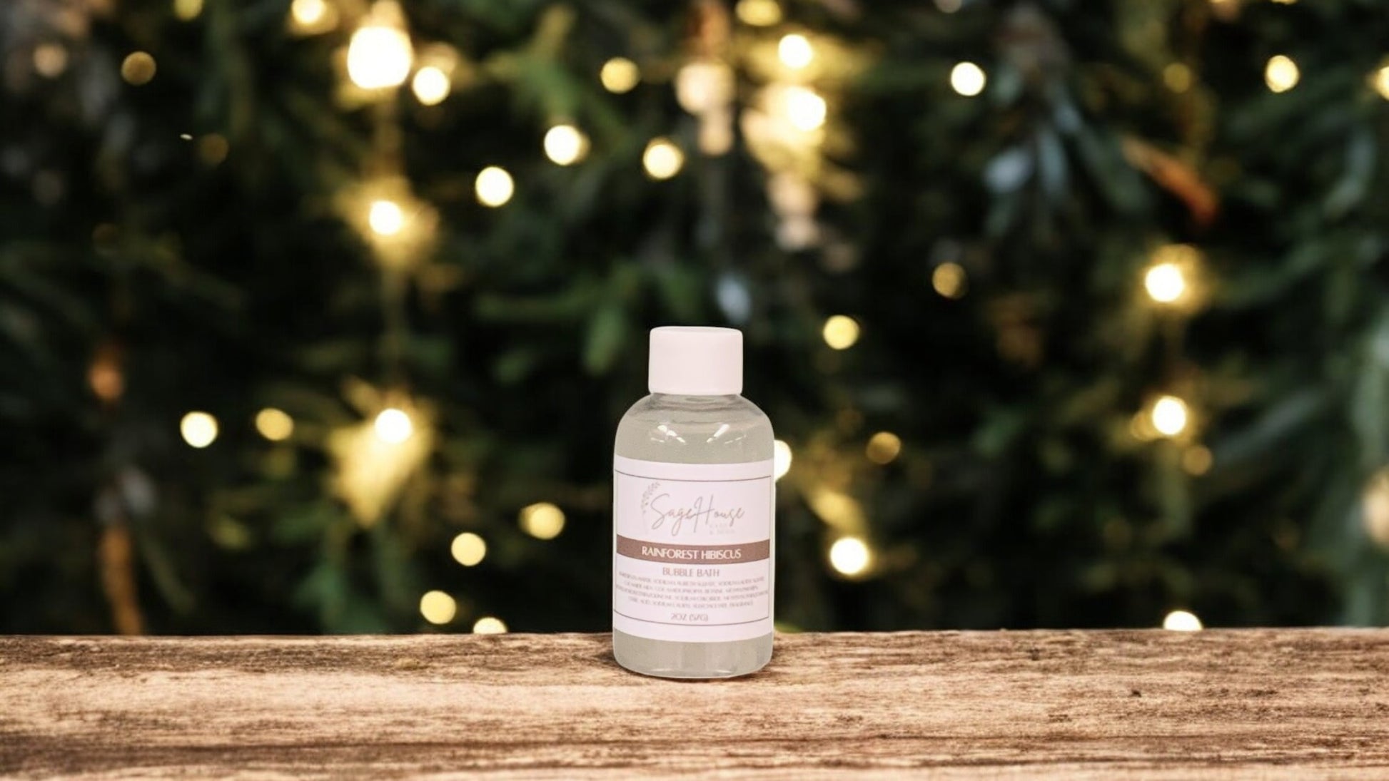 A small bottle of bubble bath, with white lid. On a wood top with greenery in the background.