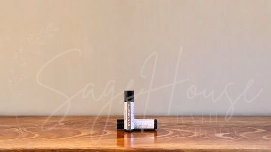 A tube of raspberry glaze lip balm placed upright with a tube lying behind it, on a wooden surface.