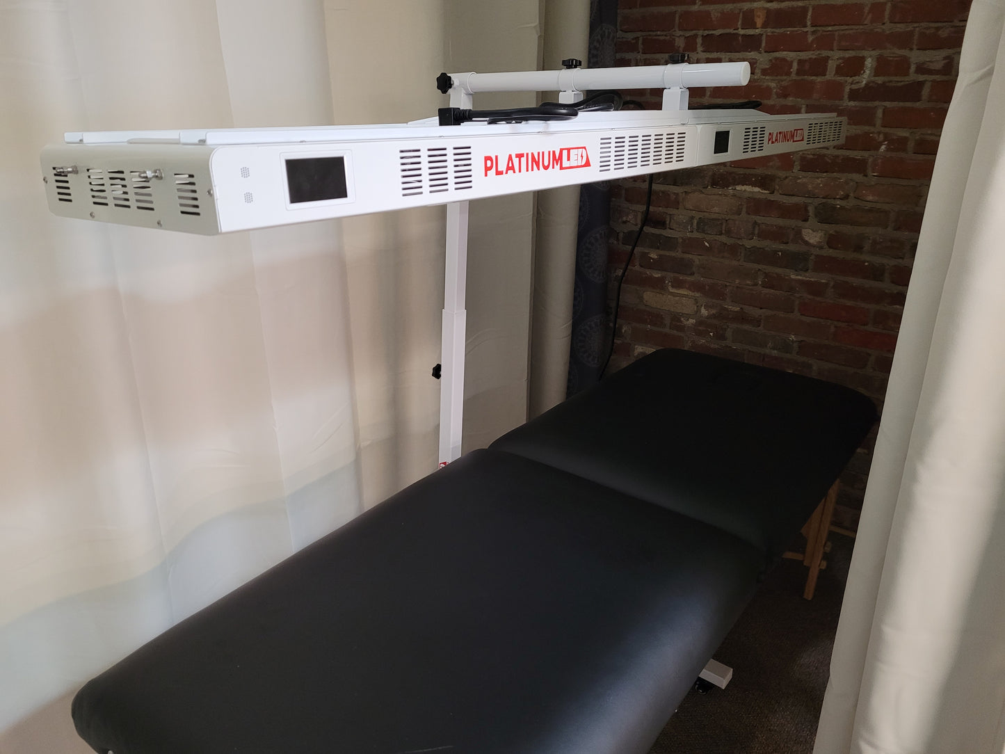 A red light therapy device mounted on a stand above a black massage table.
