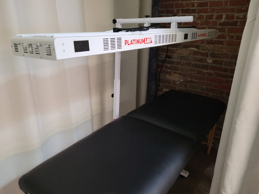 A red light therapy device mounted on a stand above a black massage table.