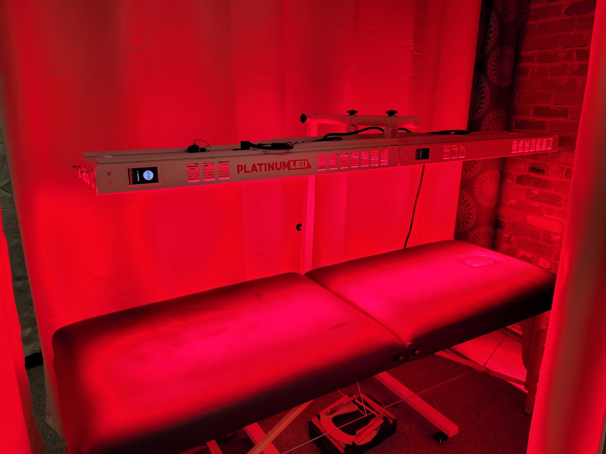 A massage table with a red light therapy machine hanging over. The light is on, so the picture is a red hue.