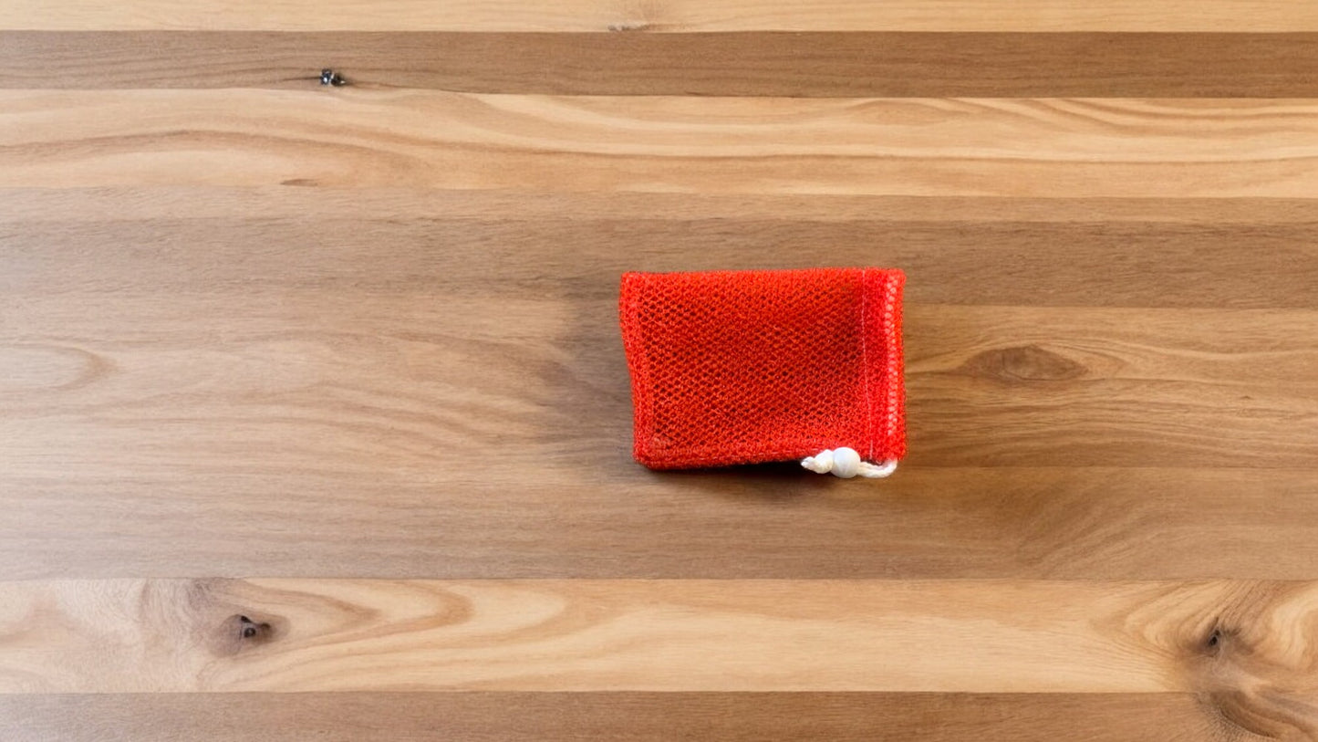 A Soap Scrub Pouch in red placed on a wooden surface.