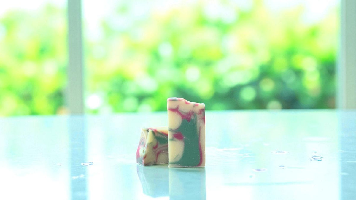 A bar of natural toned soap, with accents of green and pink on a white countertop with a blurred background