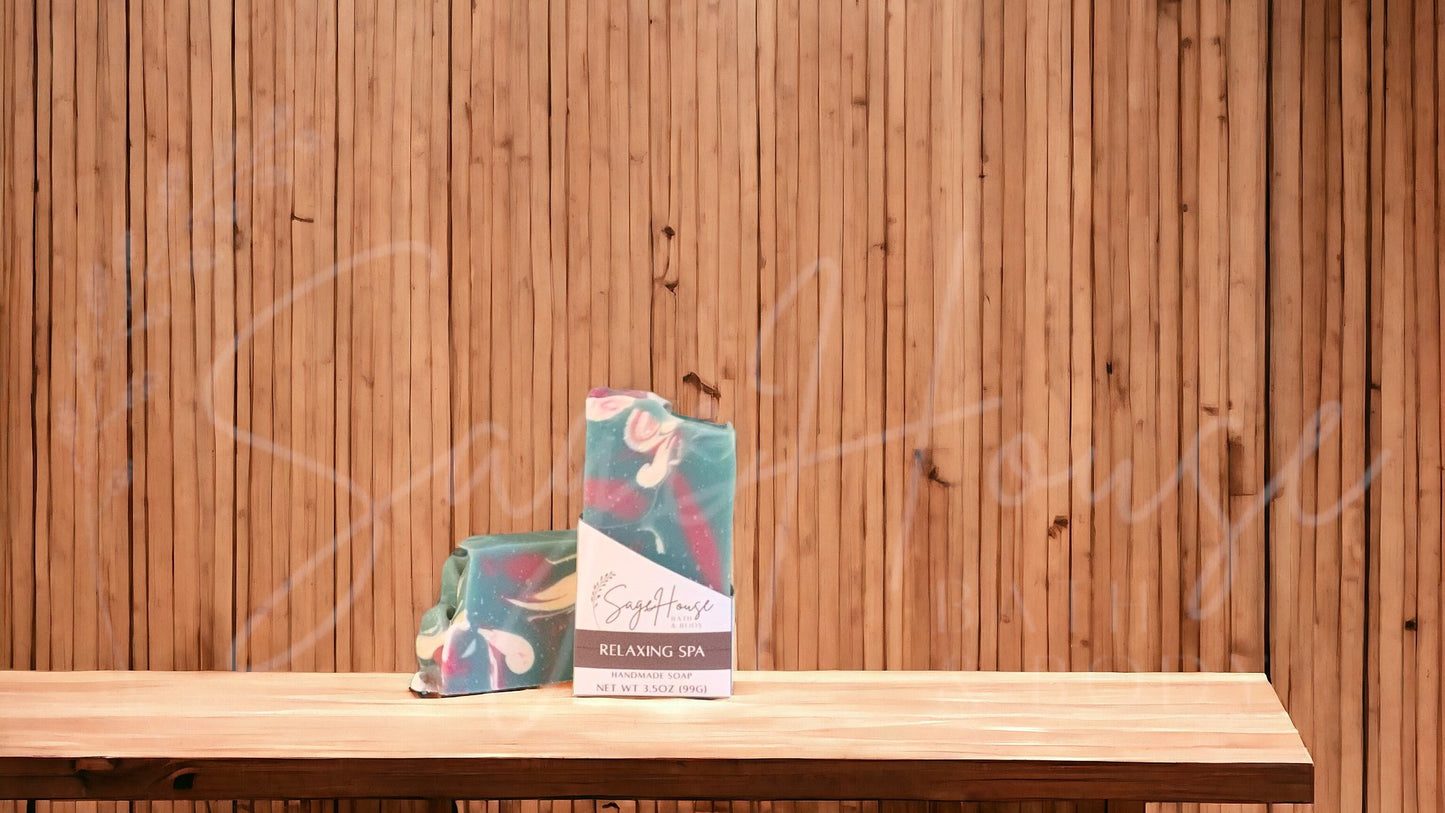 A teal colored bar of soap with accents of mauve and white, in a white labeled box, on a wood surface.