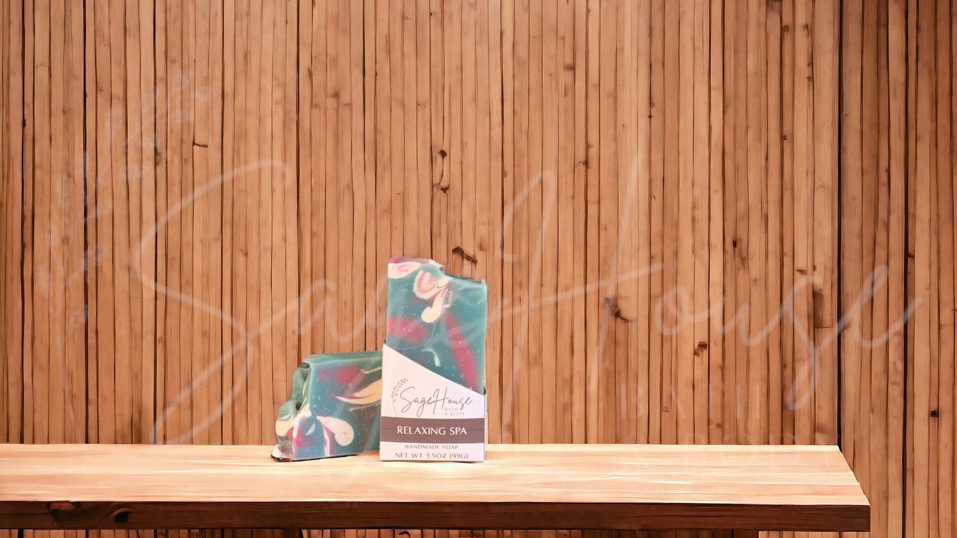 A teal colored bar of soap with accents of mauve and white, in a white labeled box, on a wood surface.