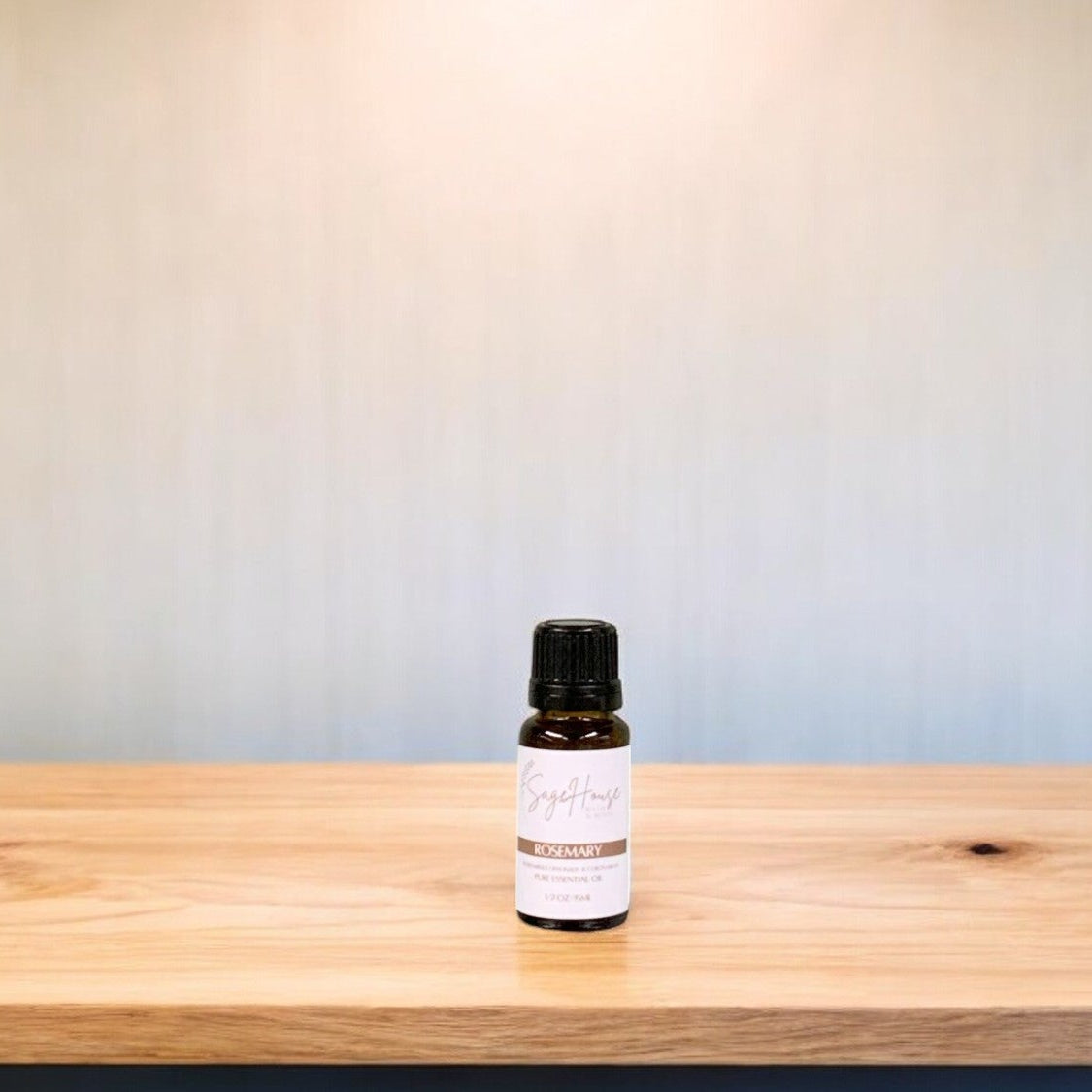 A small bottle of rosemary essential oil is placed on a wooden surface with a plain background.