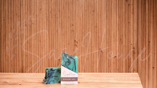A mint green colored bar of soap with black accents, in a white labeled box, on a wood surface.
