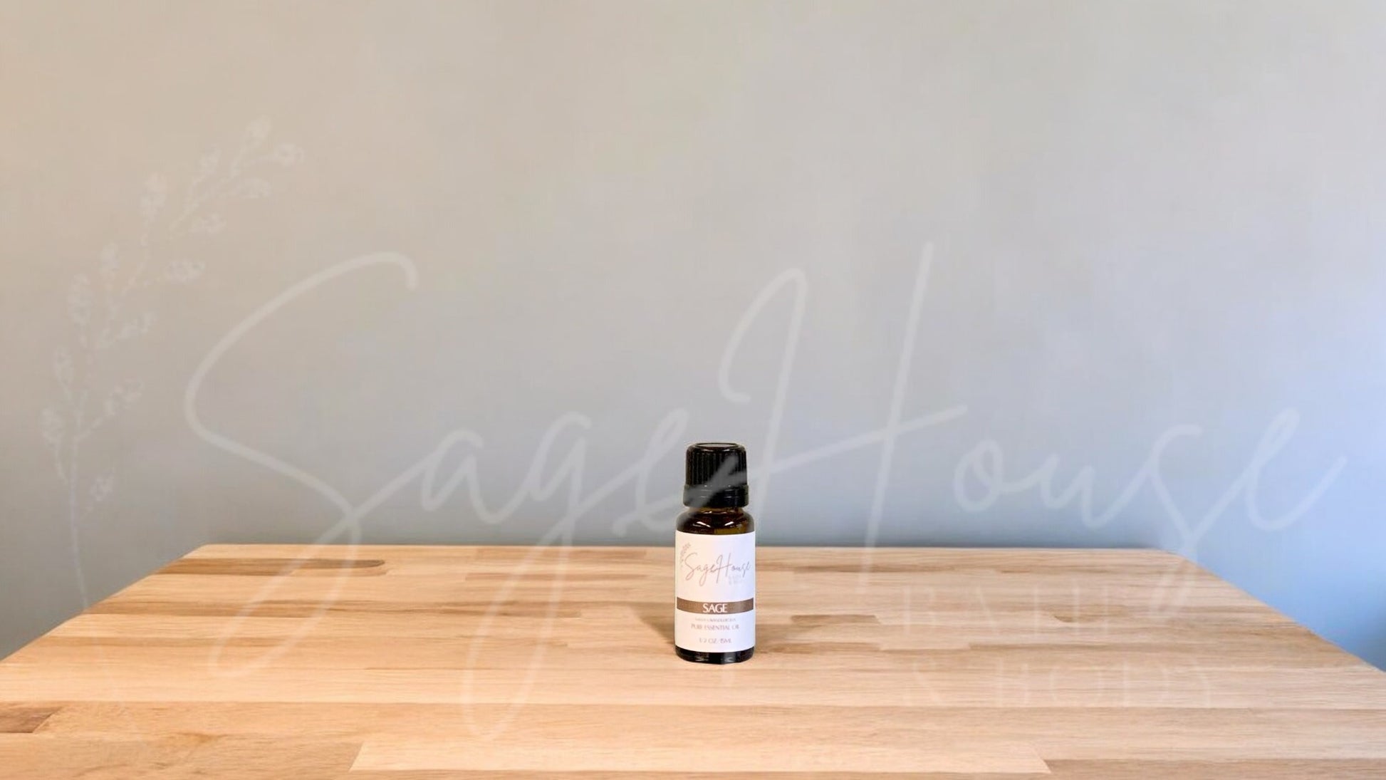 A small bottle of sage essential oil is placed on a wooden surface with a plain background.