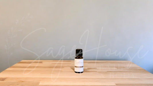 A small bottle of sage essential oil is placed on a wooden surface with a plain background.