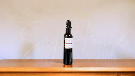 Black spray bottle with a label, on a wooden surface against a white textured wall.