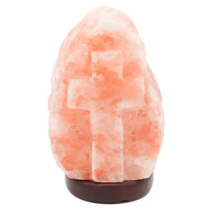 A salt lamp with a carved out cross in the middle. Sitting on a dark wood base.