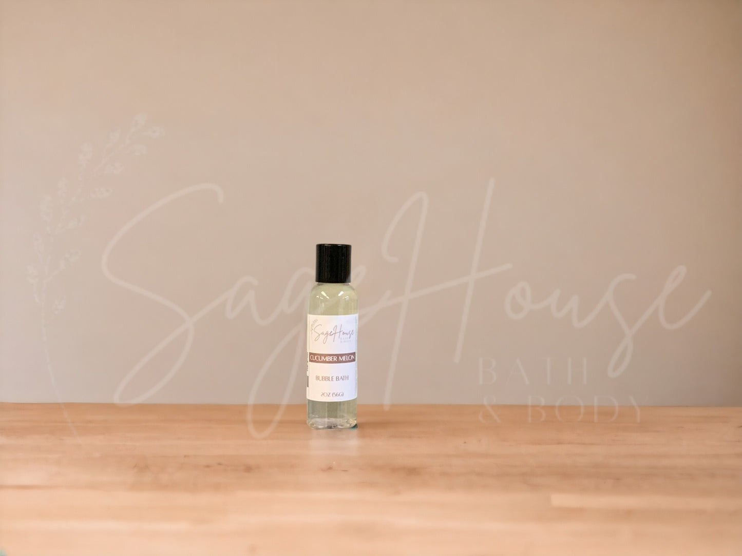 A bottle of Sage House bubble bath, labeled 'cucumber melon'. Placed on a wooden surface.