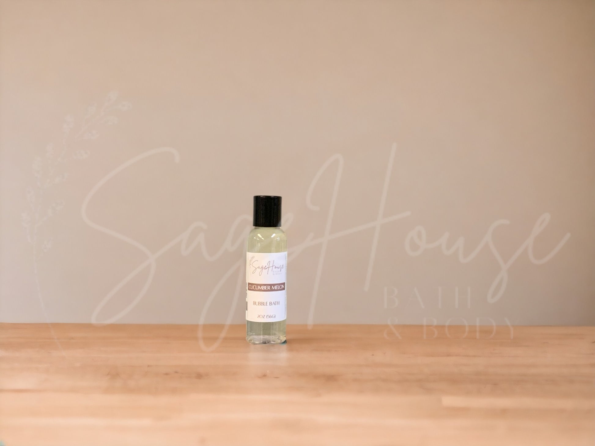 A bottle of Sage House bubble bath, labeled 'cucumber melon'. Placed on a wooden surface.