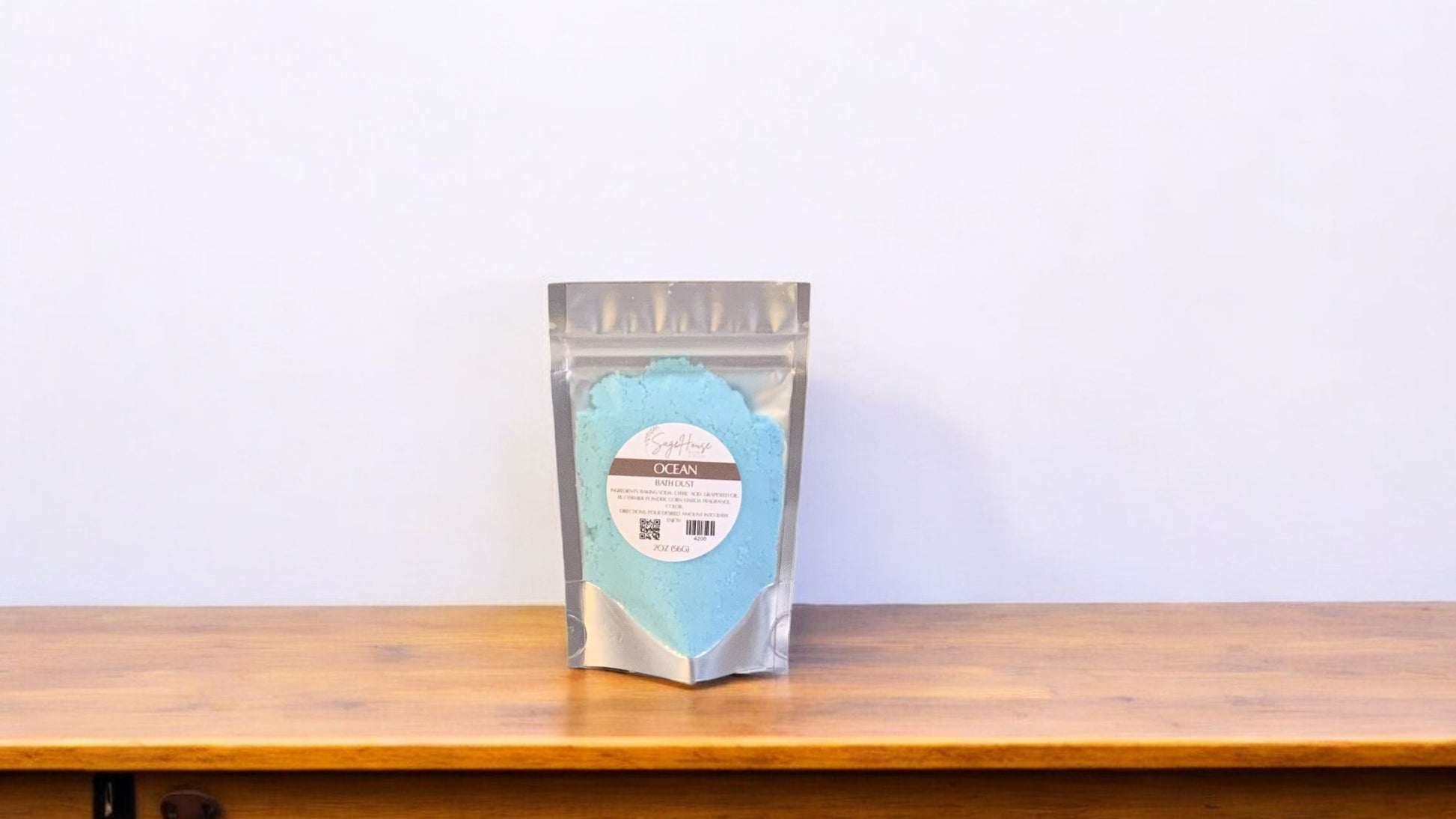 A blue-colored bath bomb in clear packaging, labeled 'ocean'. The bath bomb is placed on a wooden surface.