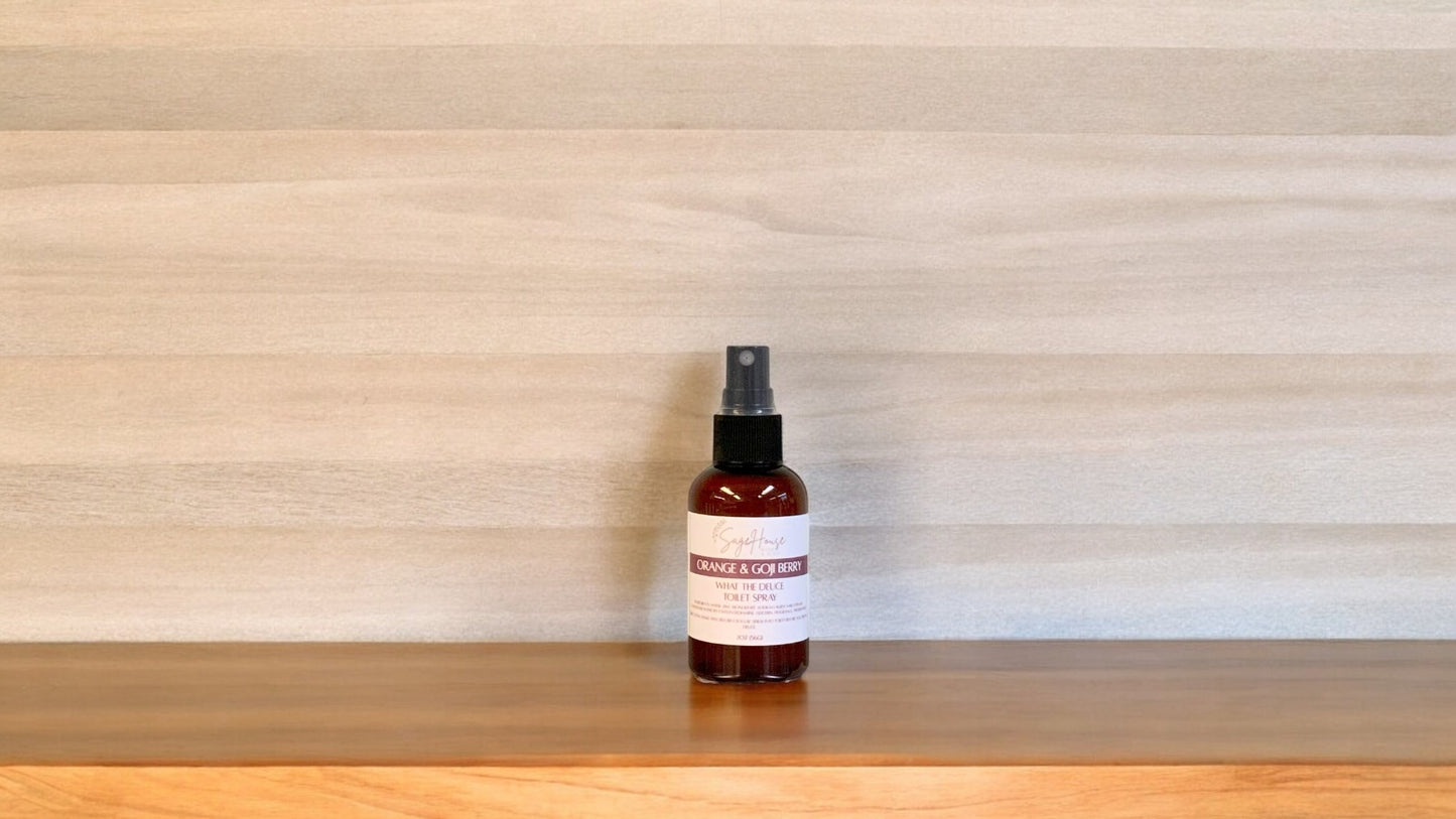 Amber colored spritz bottle with orange and goji label, on wood surface