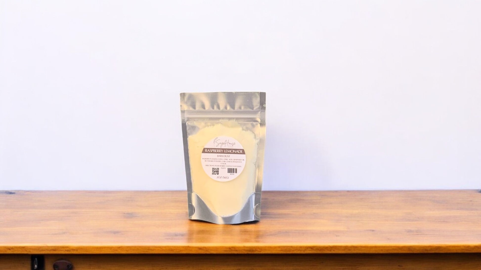 A yellow-colored bath dust in clear packaging, labeled 'raspberry lemonade'. placed on a wooden surface.