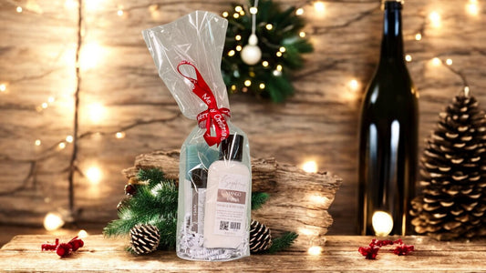 A small round giftset containing various bath and body products, tied with a red ribbon. On a wood surface with rustice theme in background